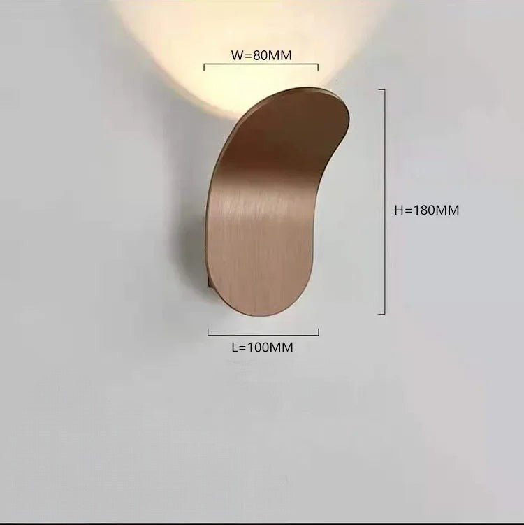 Clairly antique golden curved aluminium LED wall lamp casting a soft downward glow on a white wall