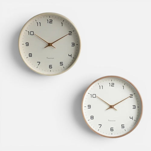 Clairly minimalist round wooden wall clocks with white dials and gold hands mounted on a grey wall.